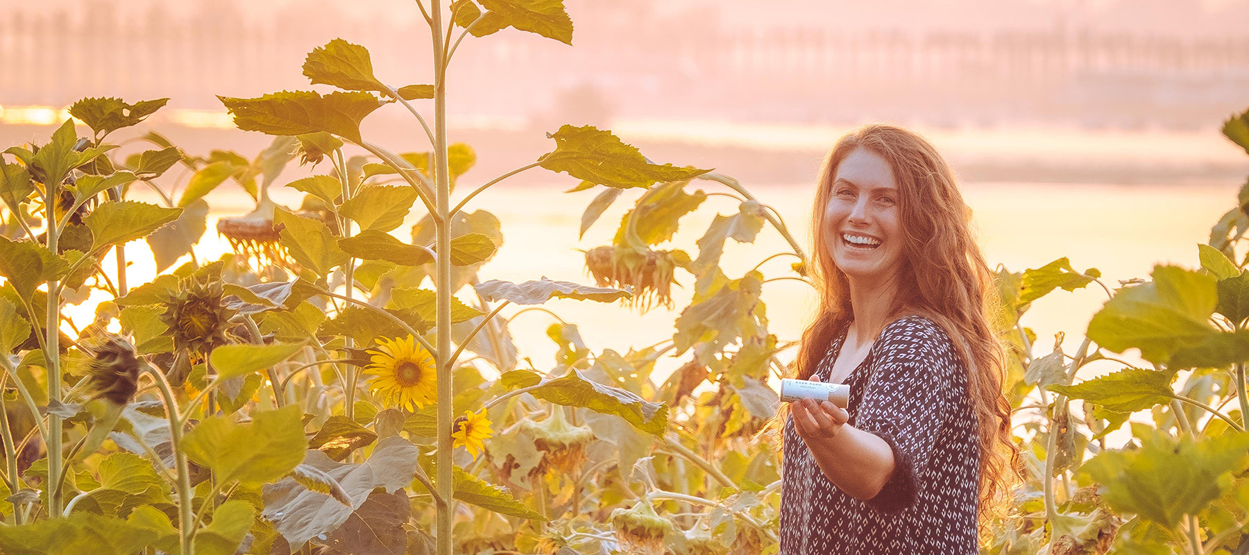 Woman in sunflower field whit ocean in the background, holding an Everkind deodorant.