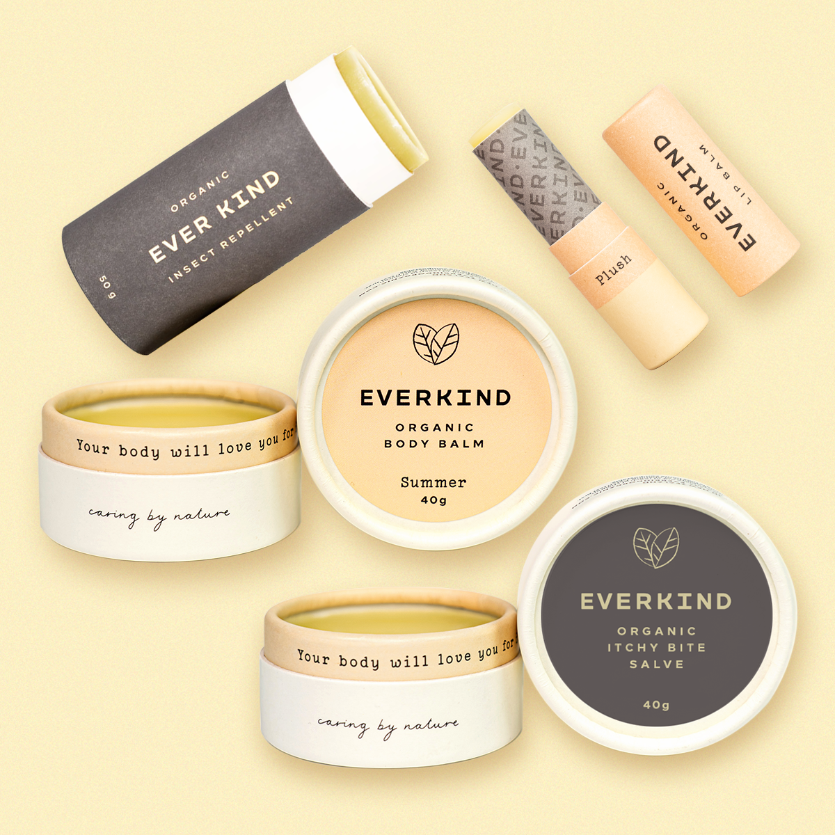 The Everkind Summer Soothe Set, featuring four certified organic products. From top left: Insect Repellent in a charcoal paper stick, Plush Lip Balm in a peach-toned tube, Summer Body Balm in a white paper jar with beige label, and Itchy Bite Salve in a white jar with a deep grey label. Each balm is shown open, revealing a smooth golden balm inside. The set is photographed on a warm, light yellow background.
